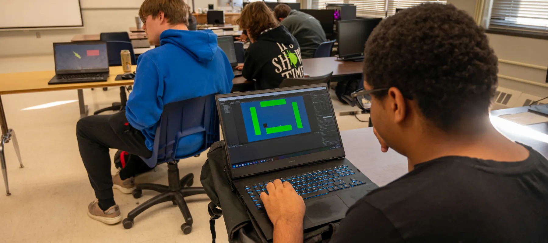 Student sitting in classroom working on building video game on laptop.