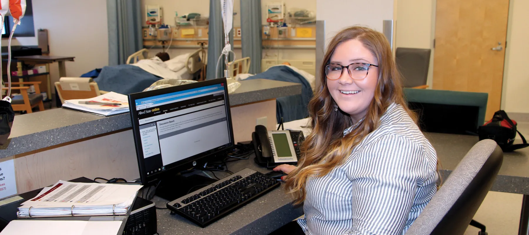 Student sitting at counter in front of computer in hospital environment.