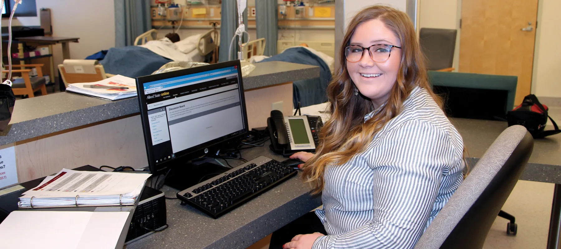 Student sitting at counter in front of computer in hospital environment.