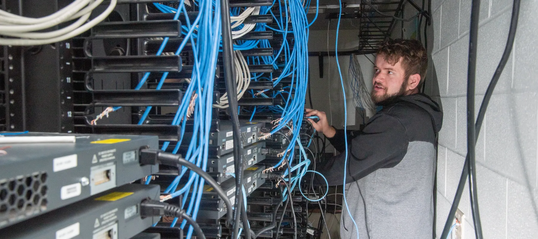 Student behind rack connecting ethernet cables in lab.