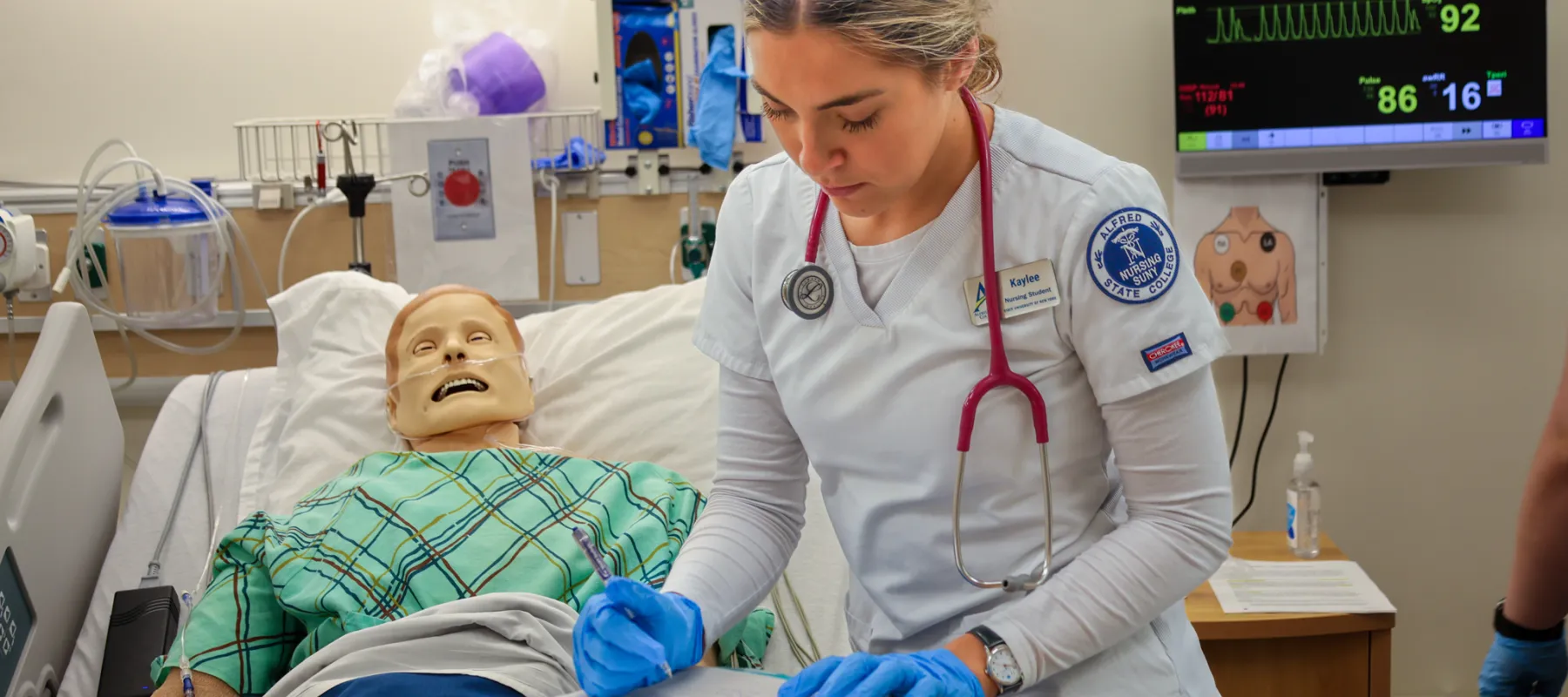 Nursing student taking notes in practice hospital environment.