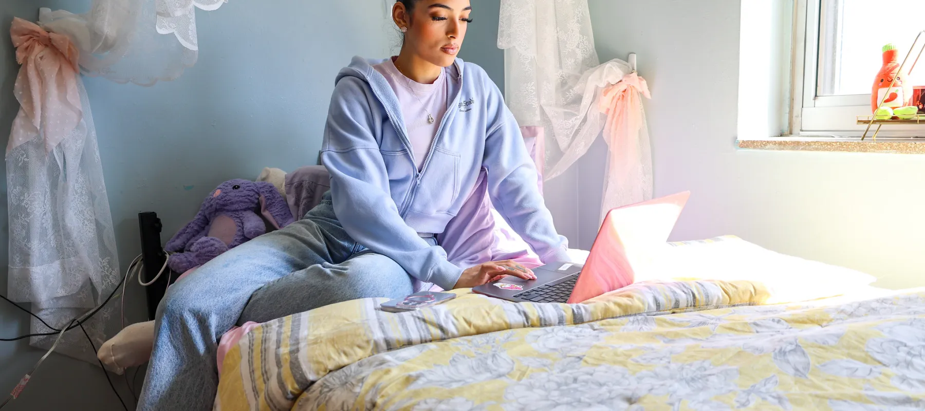 A student in a dorm room working on a laptop