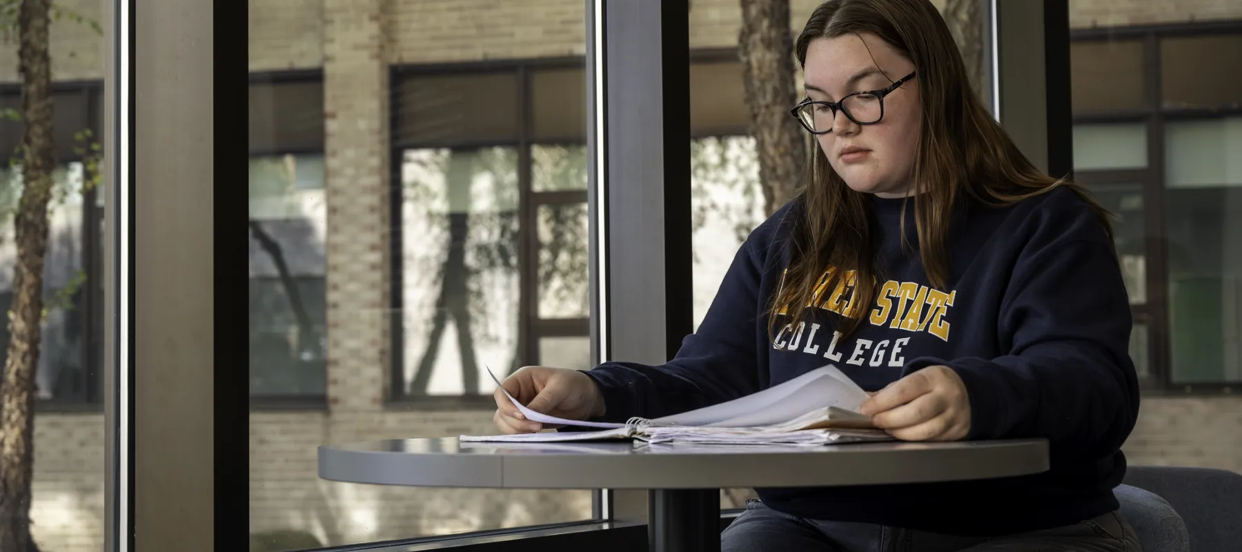 A student looking through papers in front of large windows.