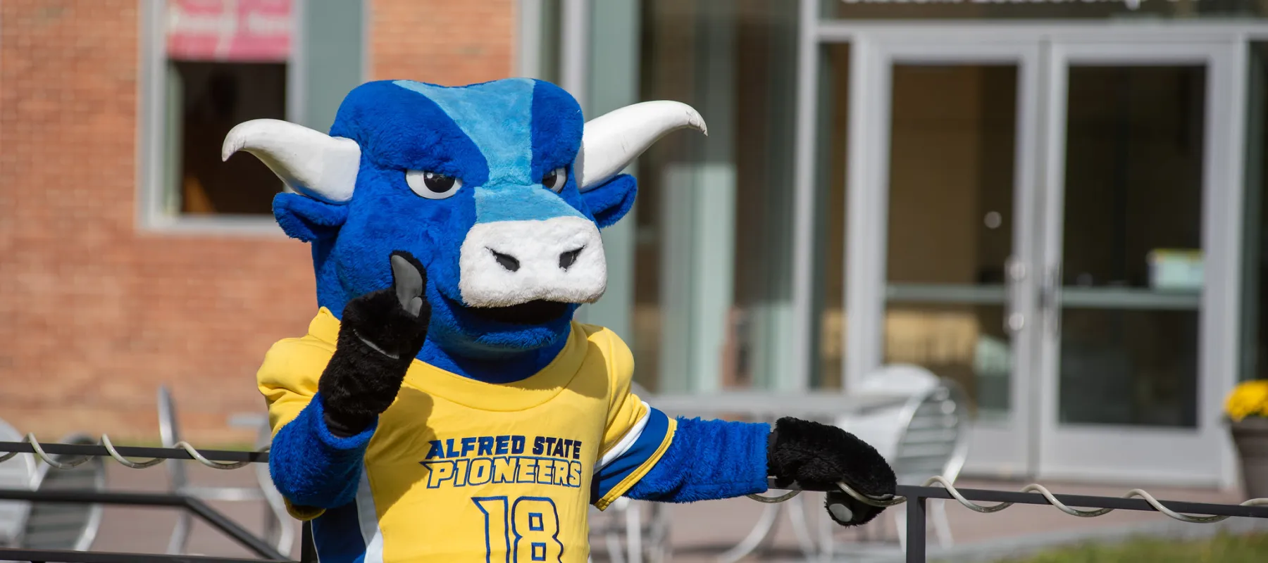 Alfred State's mascot standing outside holding up his index finger signaling #1.