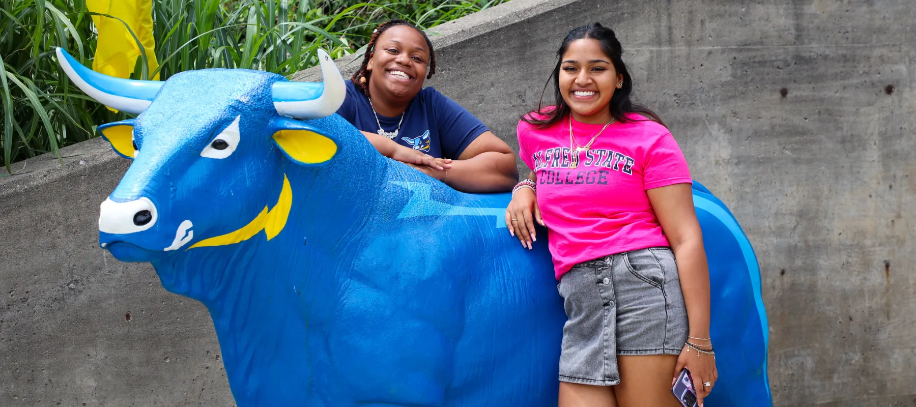 Two students standing near a statue of Alfred State's mascot, Big Blue.