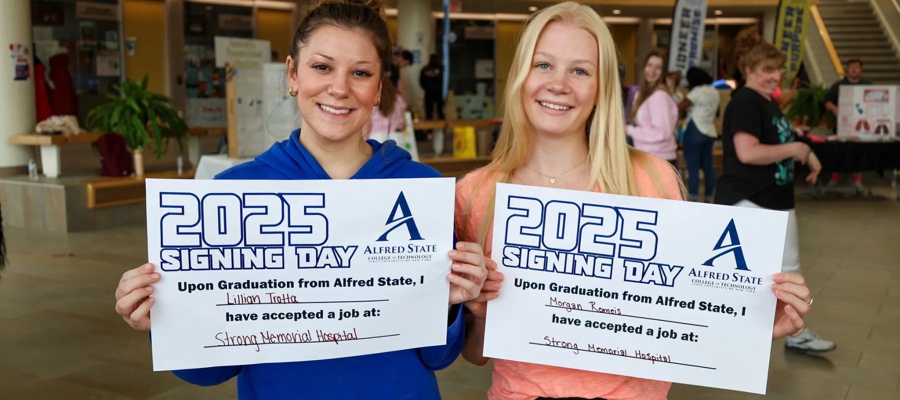 Two students holding signs that show they received jobs at a hospital after graduation