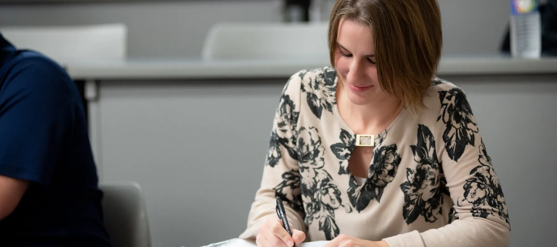 A female student writing in her notebook in a lecture hall.