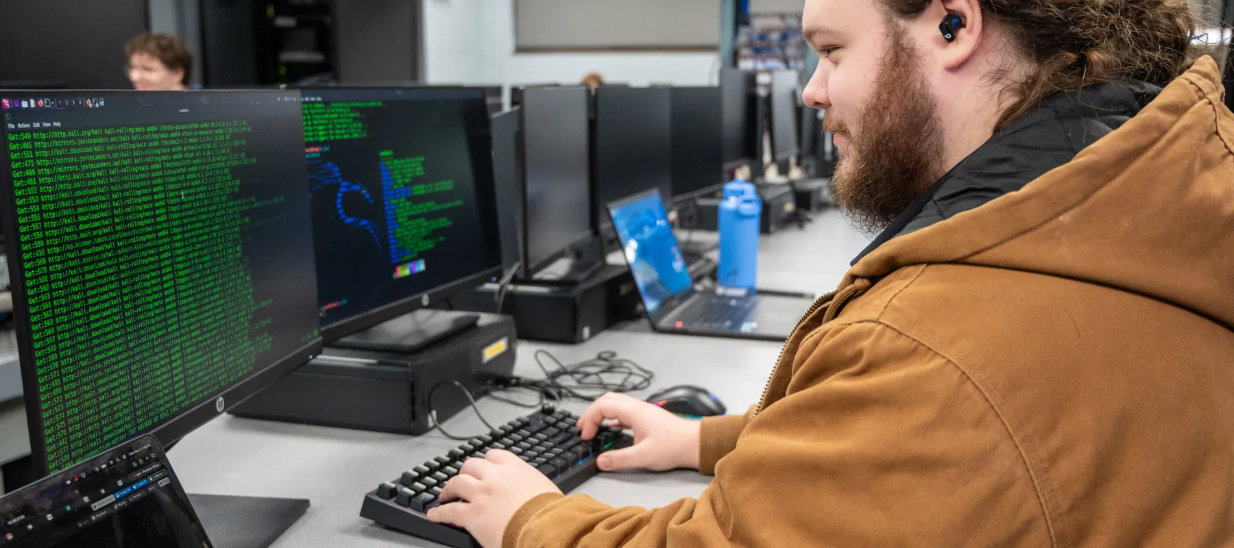 A student using a computer in a larger computer lab. The screen shows green lines of code.