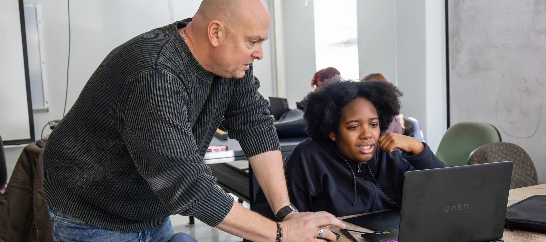 A student using a computer while receiving advice form a professor.