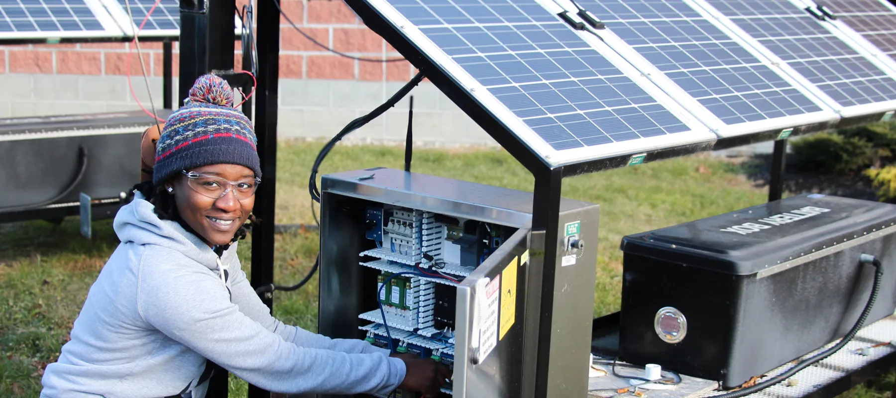 A student wearing a beanie and sweater while working on a solar panel.