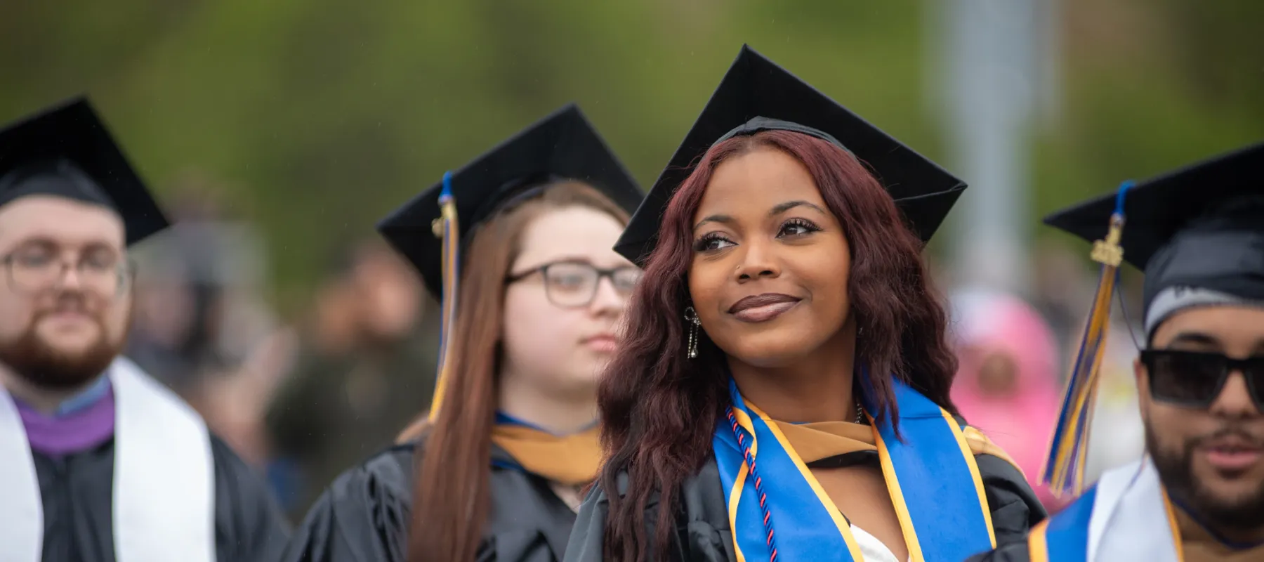 A student at graduation wearing a cap and gown while staring into the distance.