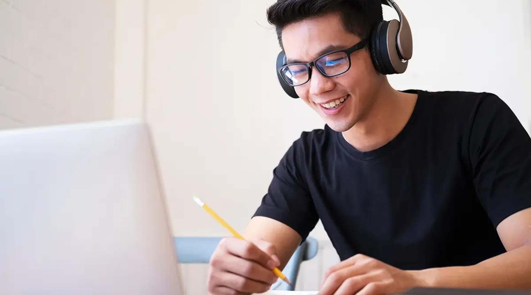 Online student sitting in front of laptop and wearing headphones taking notes.