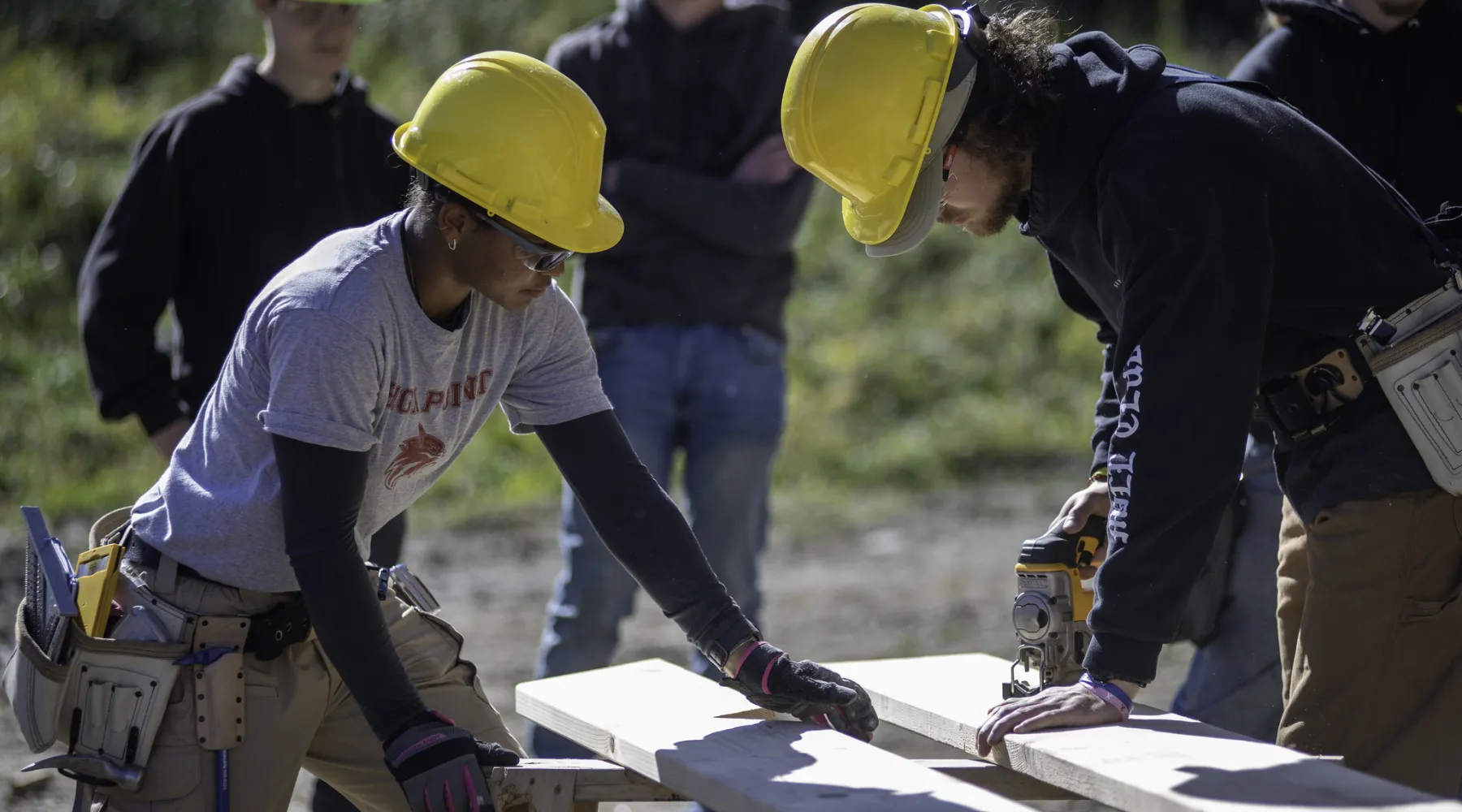 Two students cutting boards on a construction site.