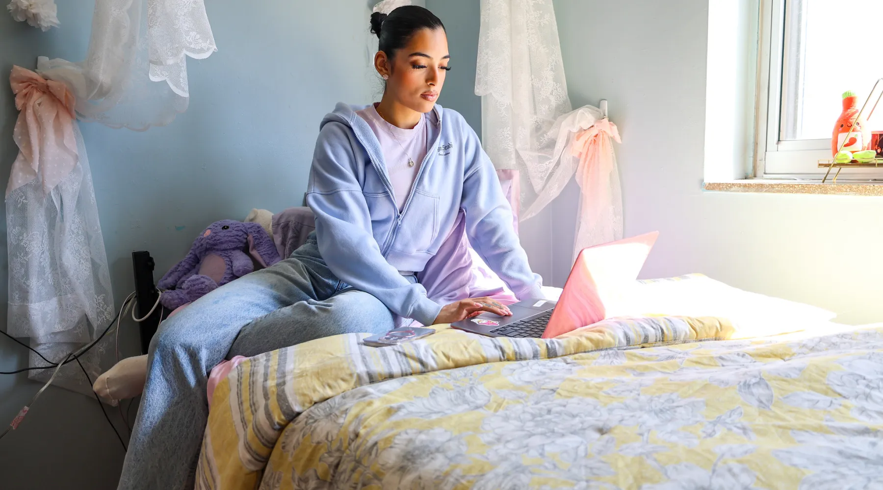 A student in a dorm room working on a laptop