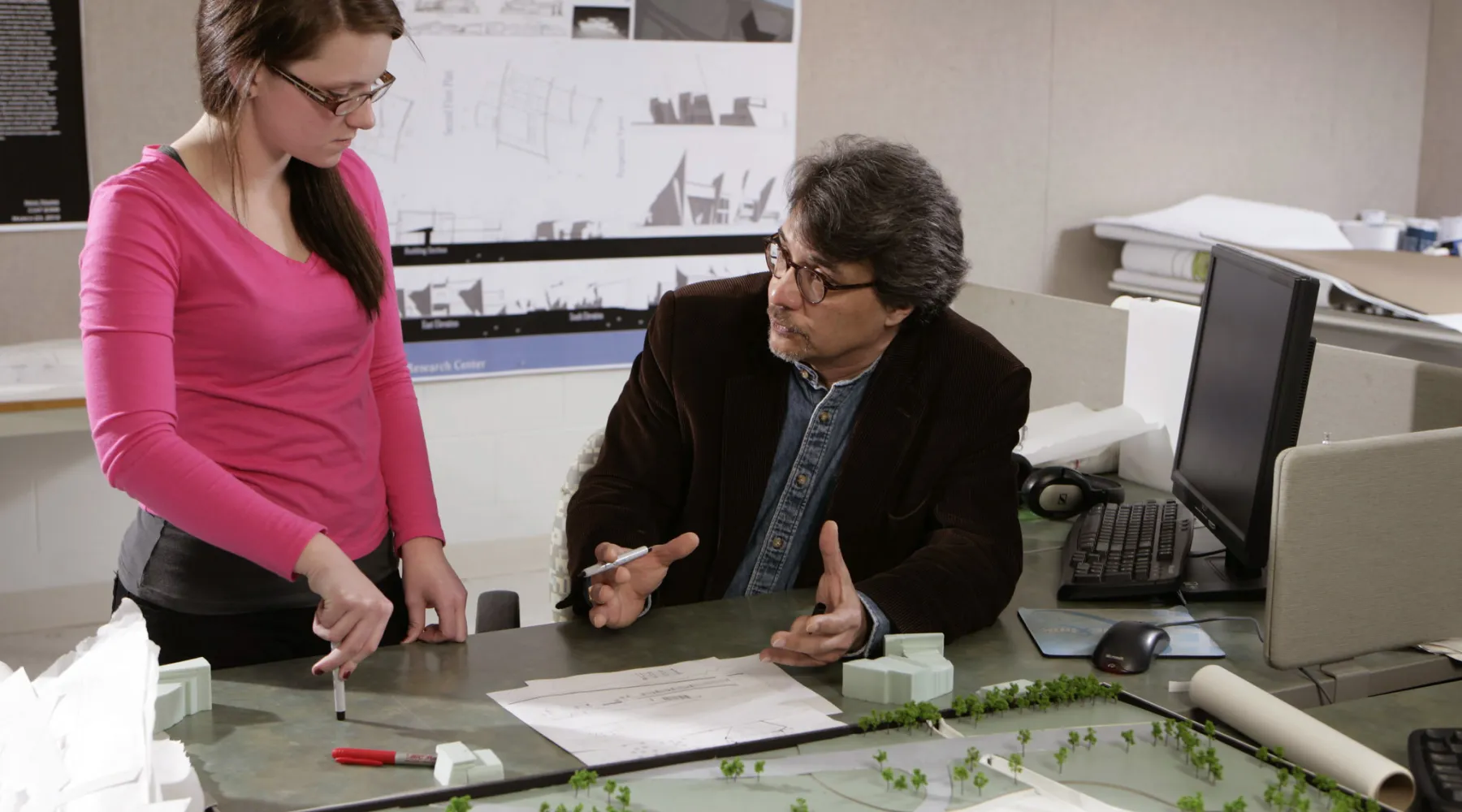 A professor and student having a conversation in front of an architectural model