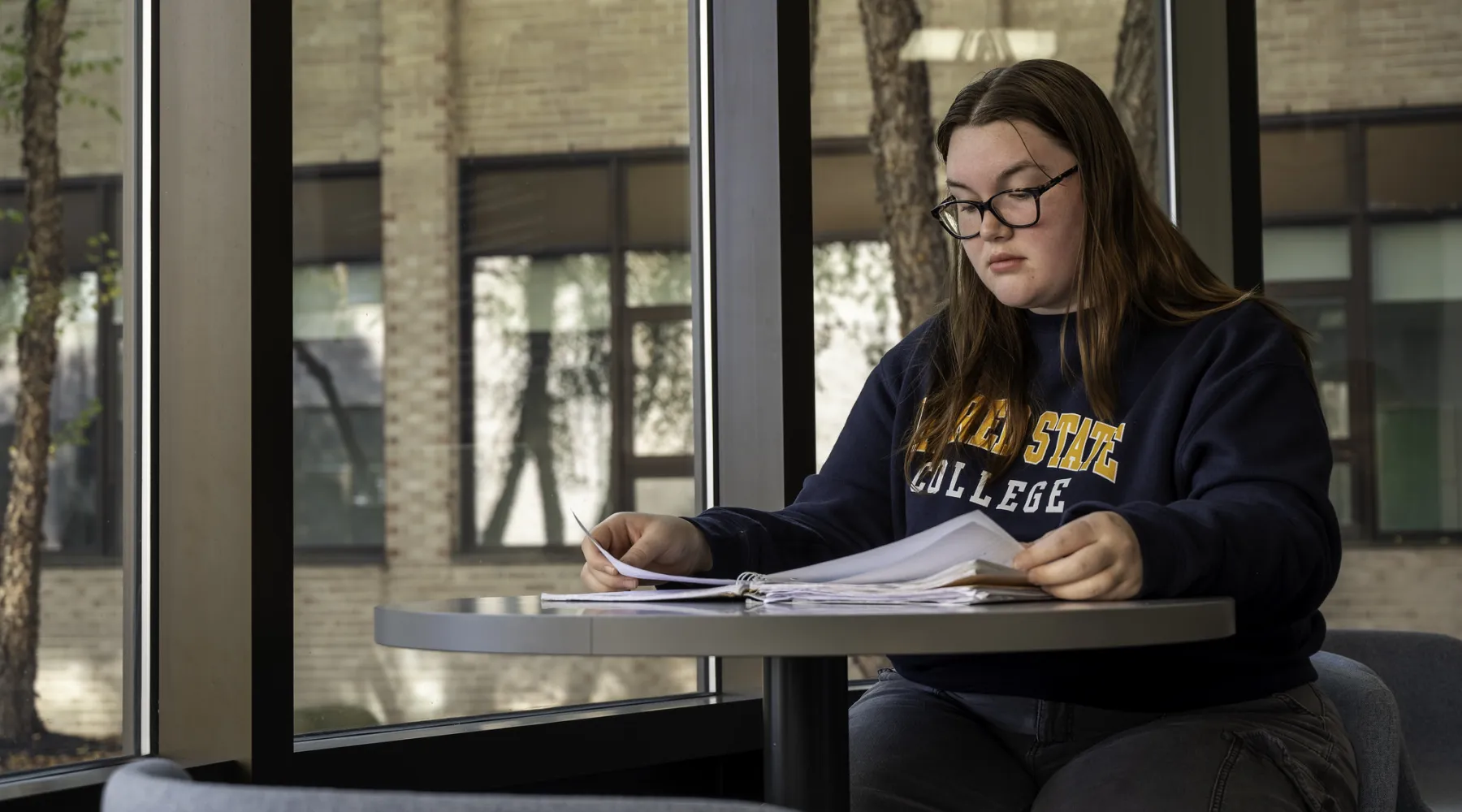 A student looking through papers in front of large windows.