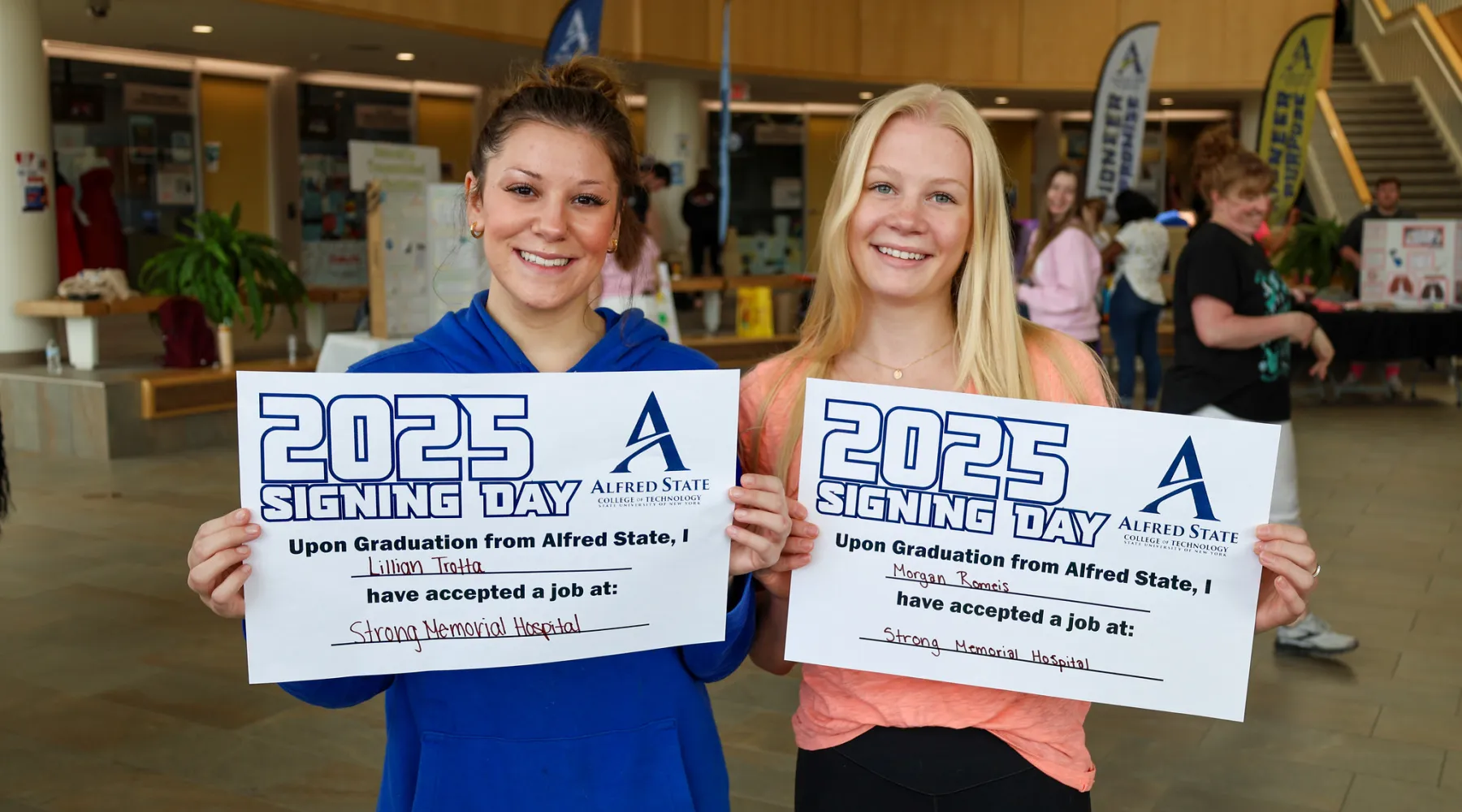 Two students holding signs that show they received jobs at a hospital after graduation
