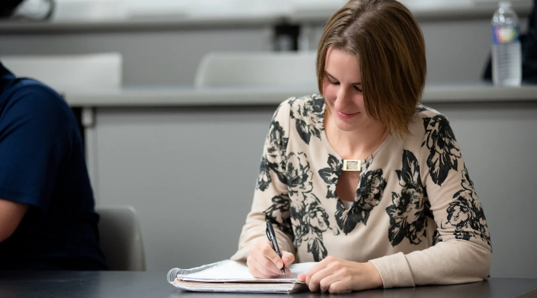 A female student writing in her notebook in a lecture hall.