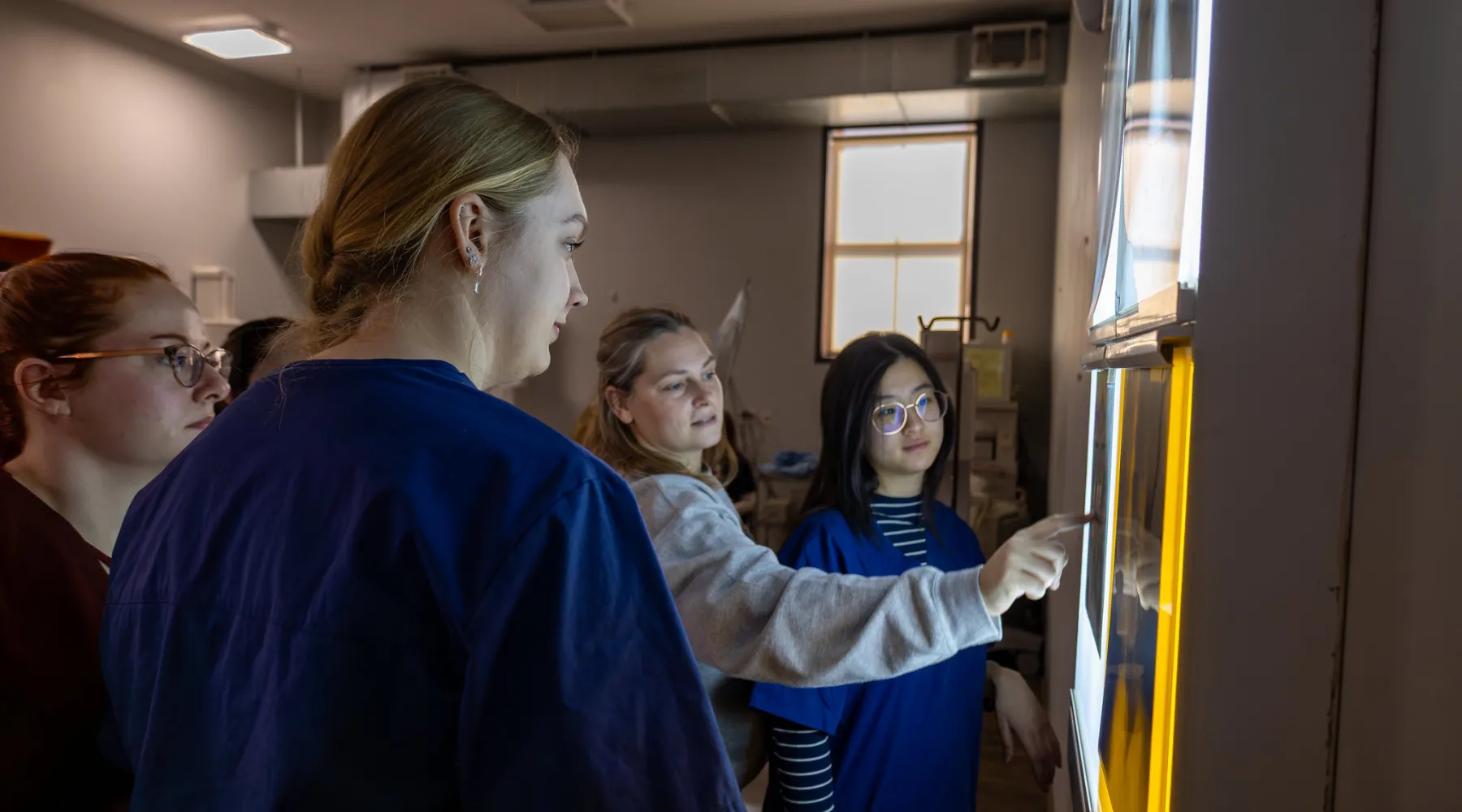 Students looking at x-rays hanging on a light wall while a professor points towards the x-rays.