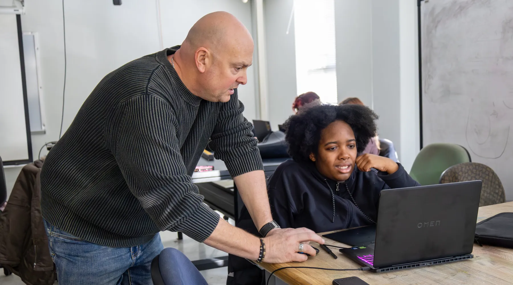 A student using a computer while receiving advice form a professor.