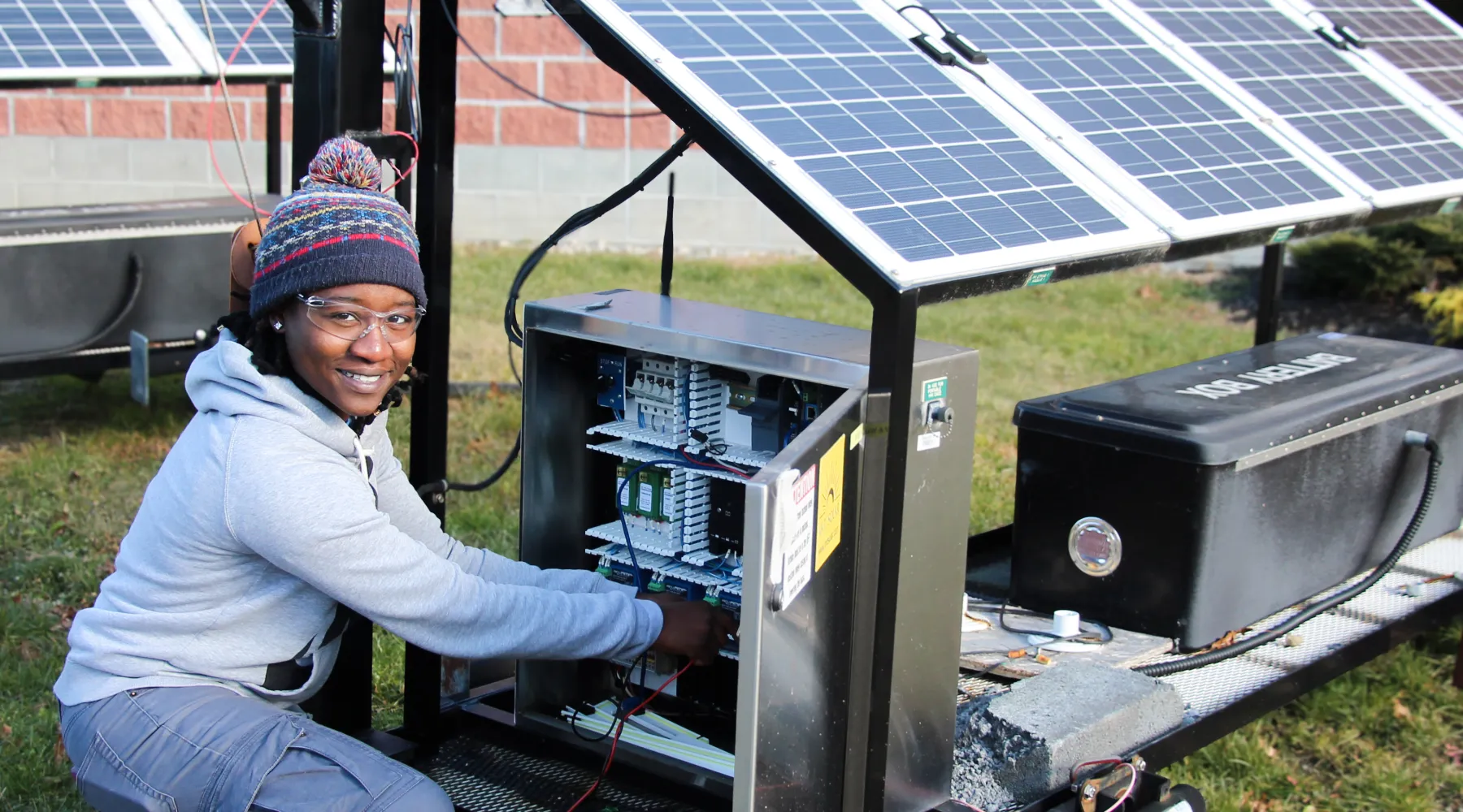 A student wearing a beanie and sweater while working on a solar panel.
