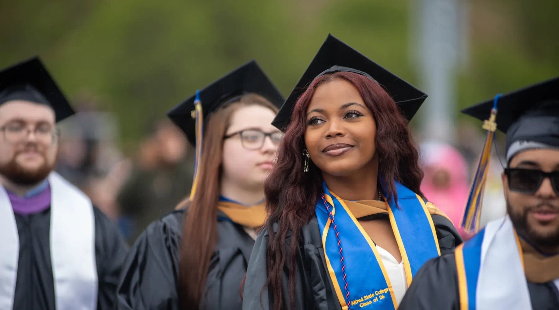 A student at graduation wearing a cap and gown while staring into the distance.