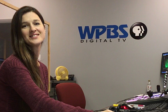 Leah sitting in front of a computer, WPBS logo on wall